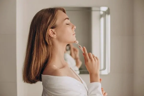Woman using facial massage roller on jawline and neck area as part of non-surgical facelift treatment routine