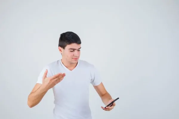 Young man in a white t-shirt looking at his phone while gesturing, symbolizing following post-operative instructions to avoid complications and encourage healing after a tummy tuck