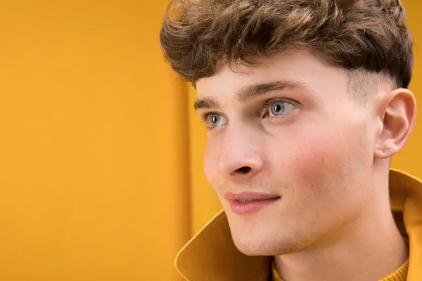 Young man with clear skin and defined jawline against yellow background, showcasing natural masculine features enhanced by PDO thread lift treatments