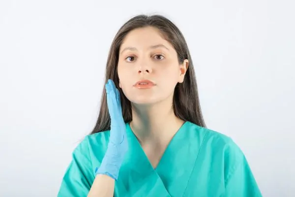 Female doctor in medical gloves showing hands on face