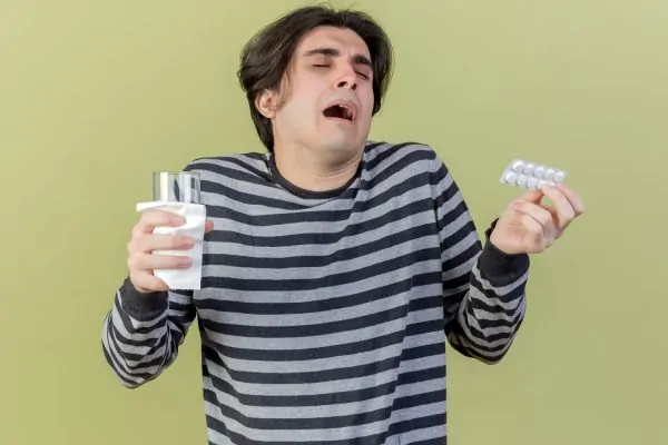 man holding pills and glass of water