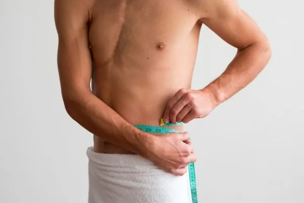 shirtless man measuring his waste with tape